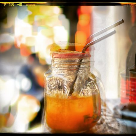Brand Marketing A jar of orange drink with a straw, blurred colourful background.